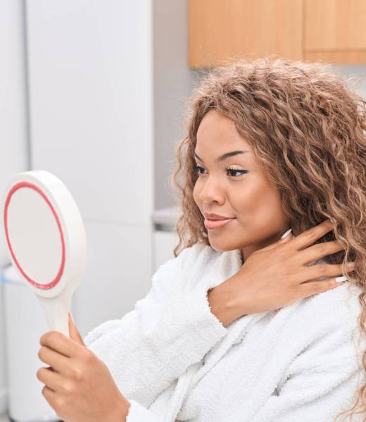 Smiling young woman in the office of a modern aesthetic medicine salon holding a round mirror in her hands